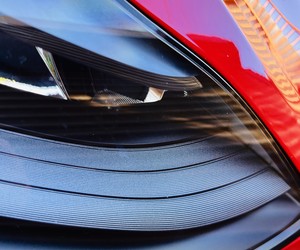 Close-up of a red car headlight with layered curves and reflections of buildings