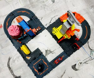 Toy racetrack with colorful buildings and miniature cars on a floor covered in drawings